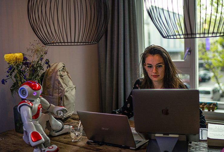 A students sits at a desk with her laptop, a small robot, and a Case Logic backpack.