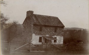 a black and white photograph of a two-story stone home with a chimney; the first story is white washed.
