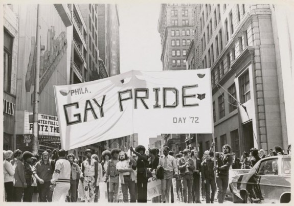 A black and white photograph of a group of people holding a large white banner with the words 
